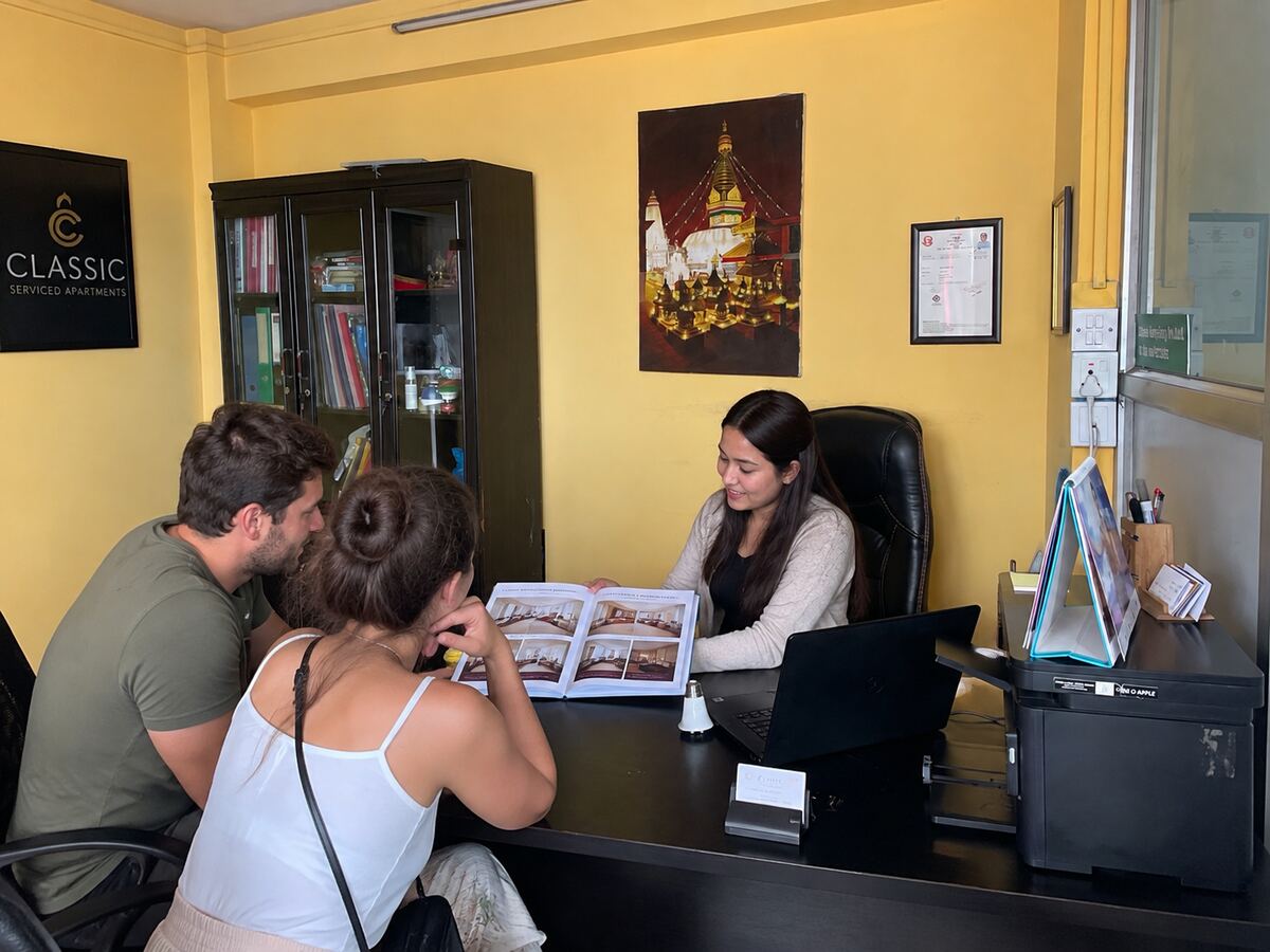 A member of staff at the welcome desk showing an apartment brochure to two guests.